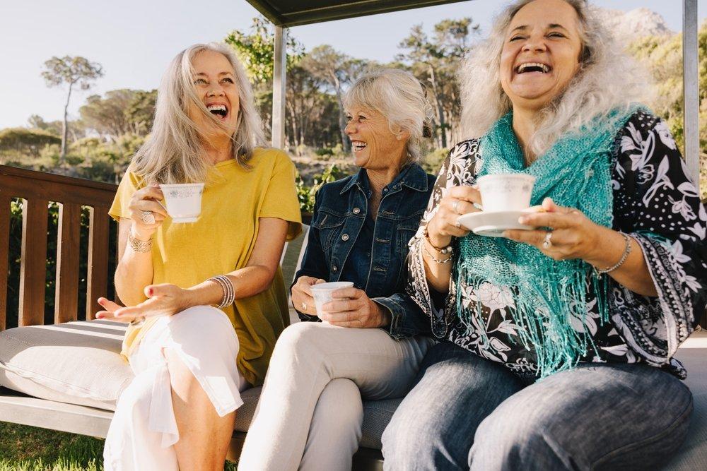 Three senior women sit outside and laugh and talk