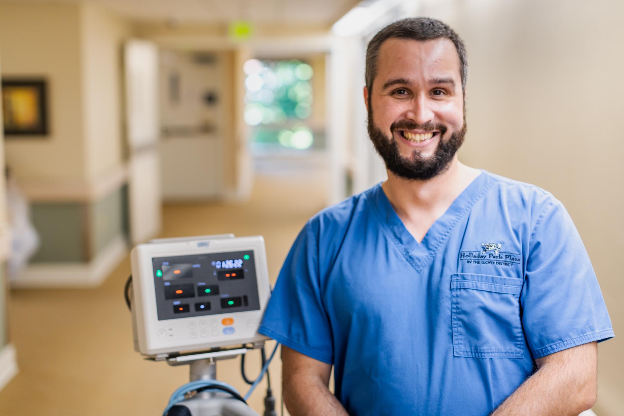A smiling healthcare employee stands by a piece of equipment.