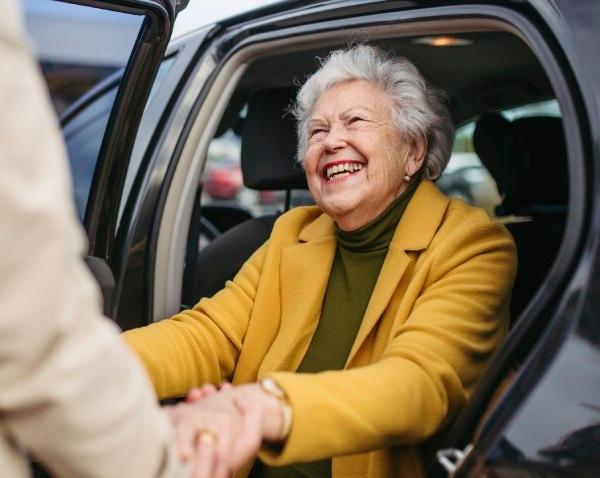 Older woman in a yellow jacket getting out of a car.
